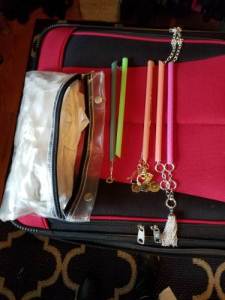 Necklaces in plastic straws to prevent them from getting tangled during travel. On top of a red suitcase with a clear plastic bag next to the necklaces
