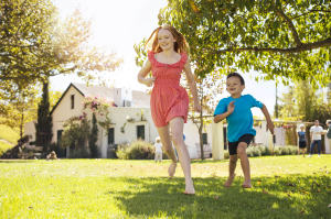 Keeping the house cool during the summer with or without air conditioning by keeping shades down and other cost effective ideas. Kids running in the backyard of a nice house.