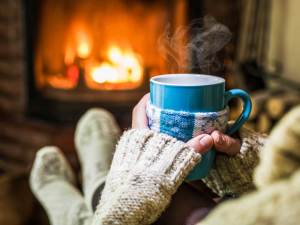 person with sweater with a hot beverage infront of a fireplace.